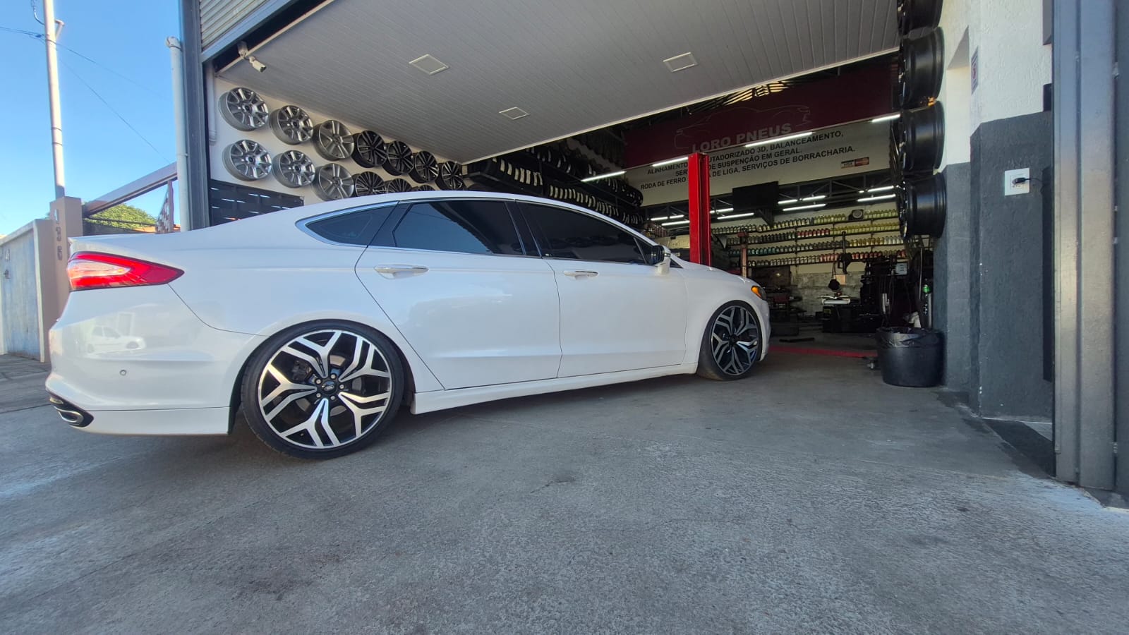 Carro branco com rodas esportivas na entrada da oficina